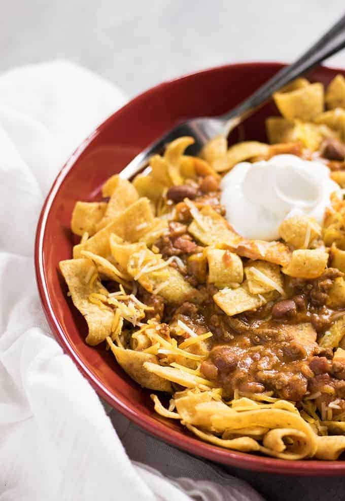 corn chips topped with chili and sour cream in a bowl.