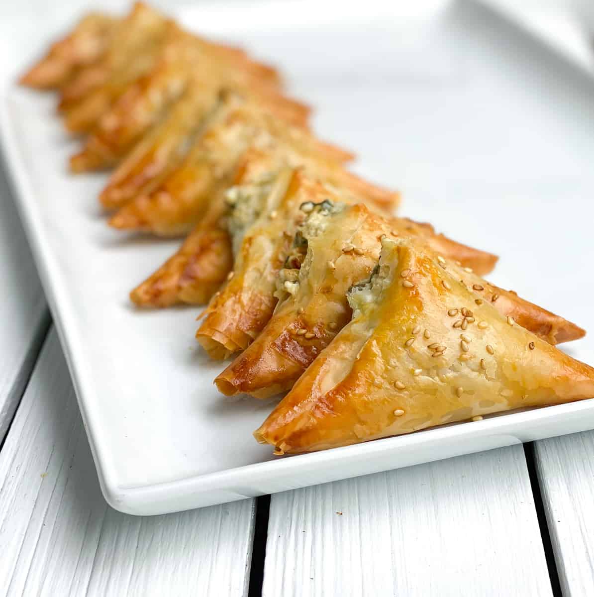 crispy mini spanakopita triangles on a white plate.