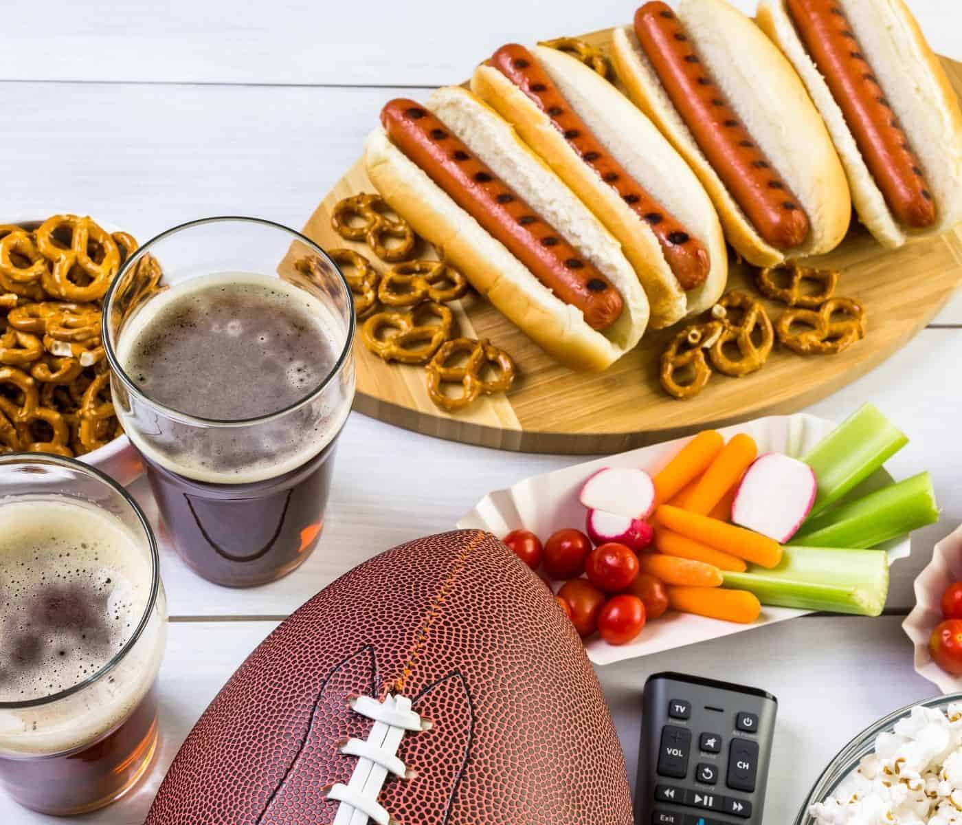 Hotdogs, beer, finger foods and a football on a table for the big game.