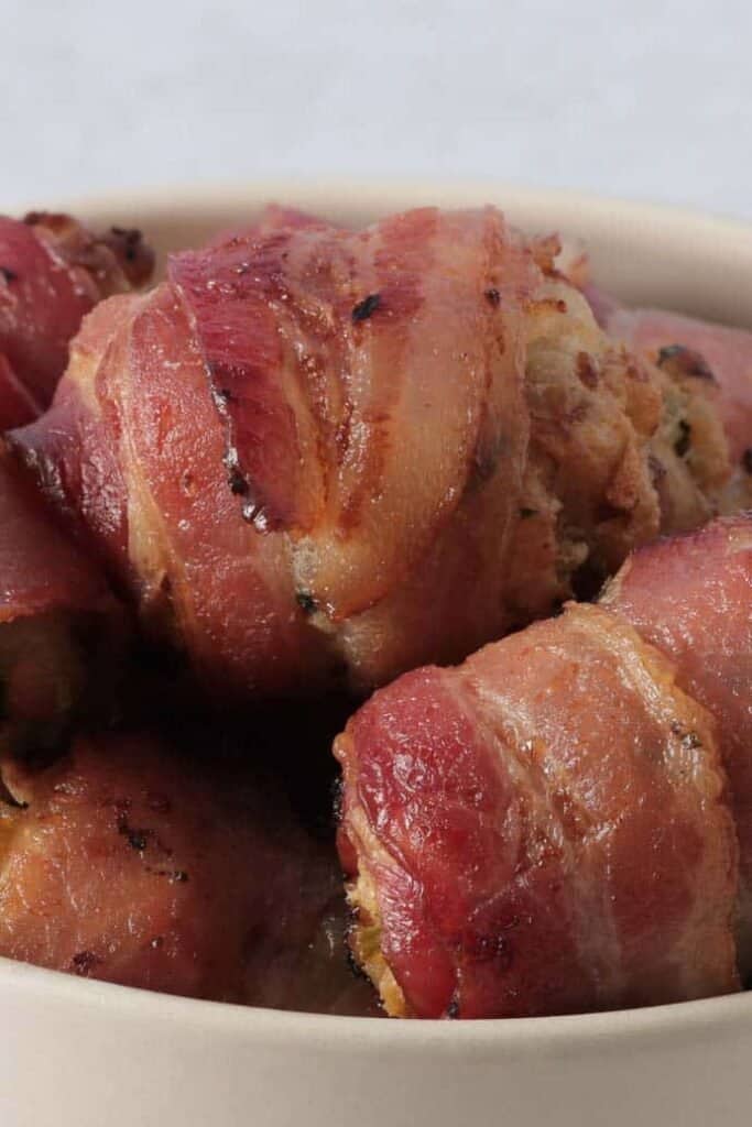 A close up of crispy, cooked bacon wrapped around a ball of stuffing.