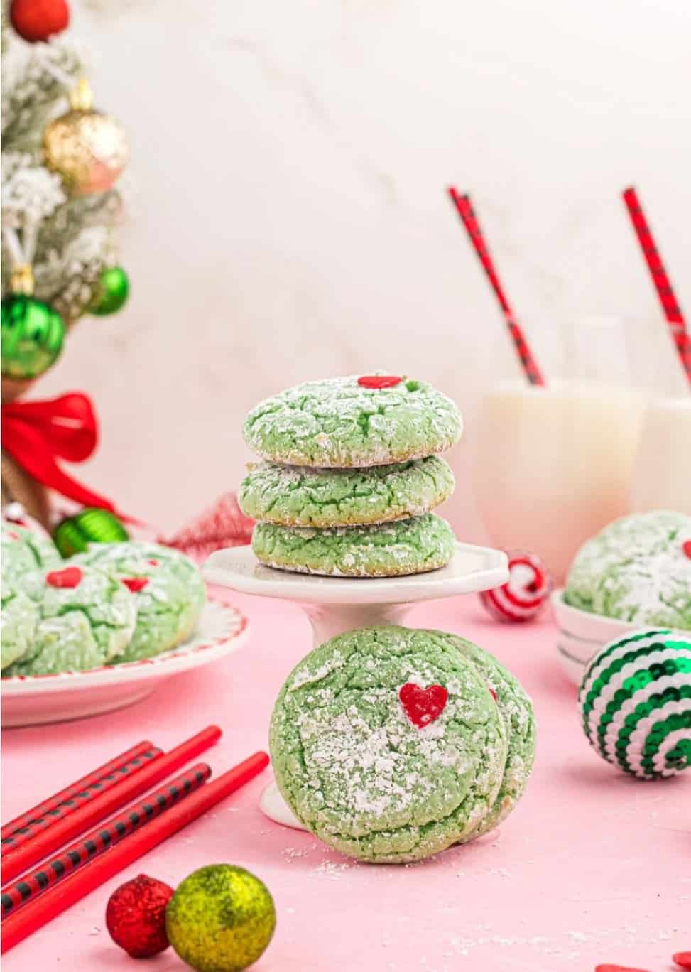 Green cookies with red hearts stacked on plates with Christmas decorations.