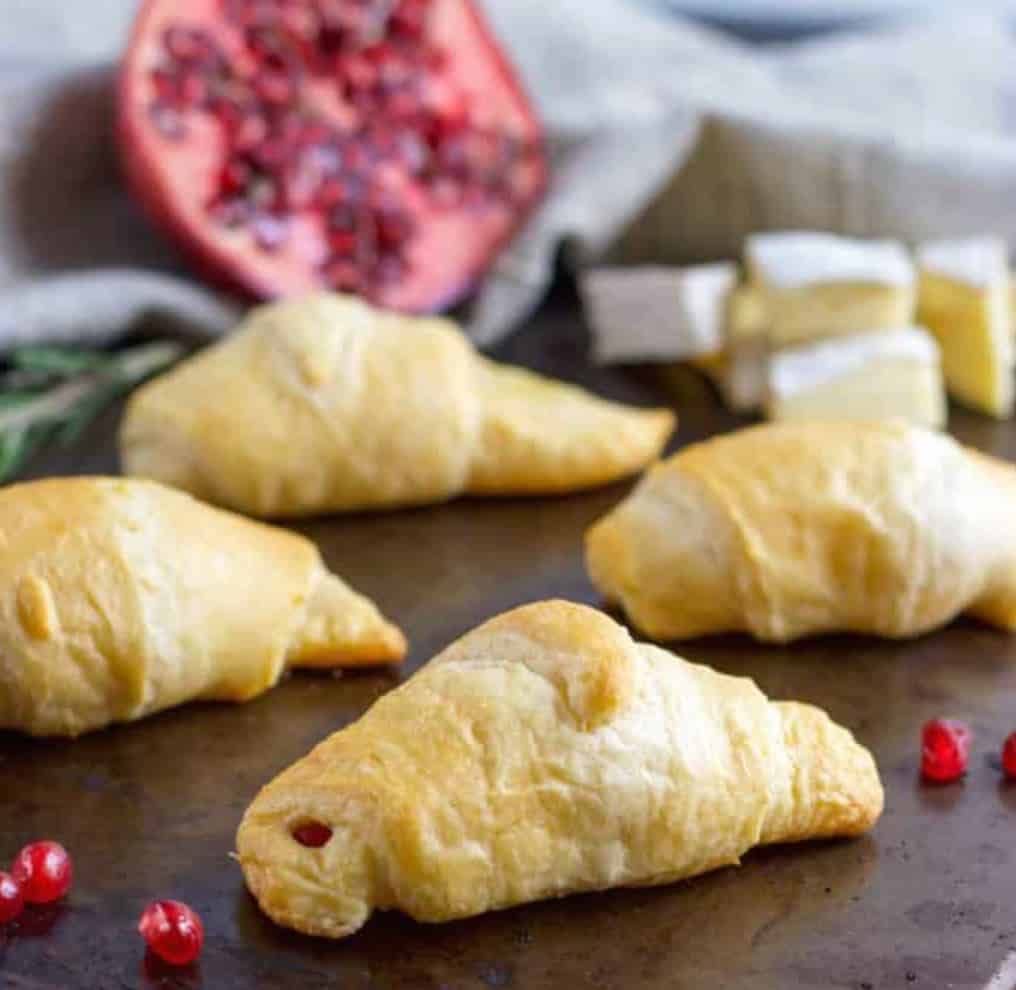 Crescent rolls on a table with a pomegrante and a blue napkin for decoration.