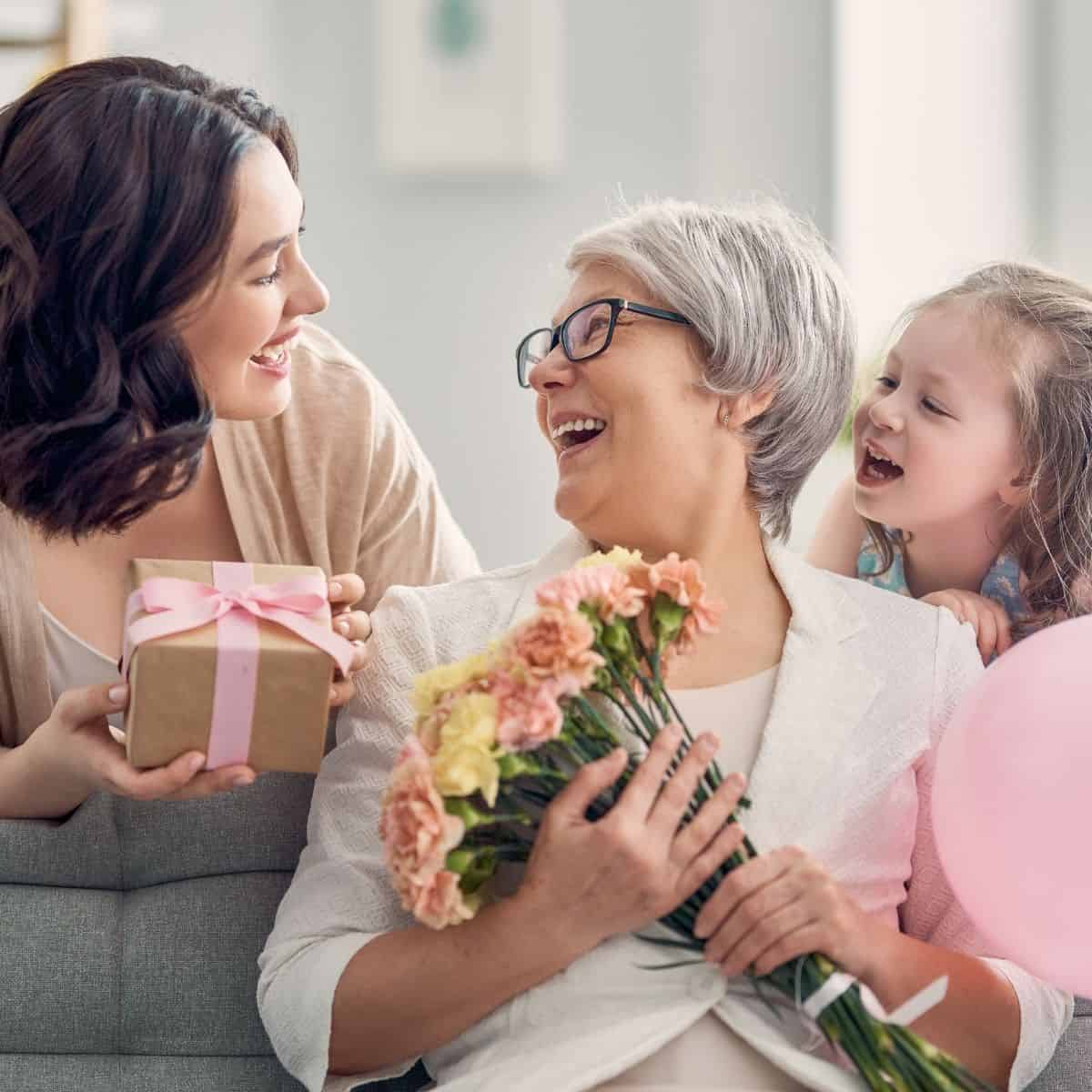 Grandmother, mother and daught on a couch with flowers and gifts.