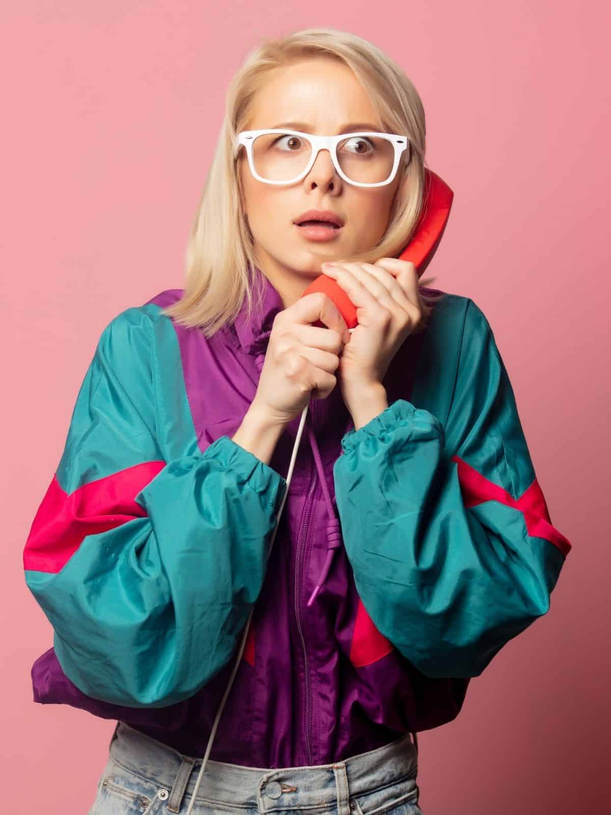 Woman on the phone with glasses and 90's jacket.
