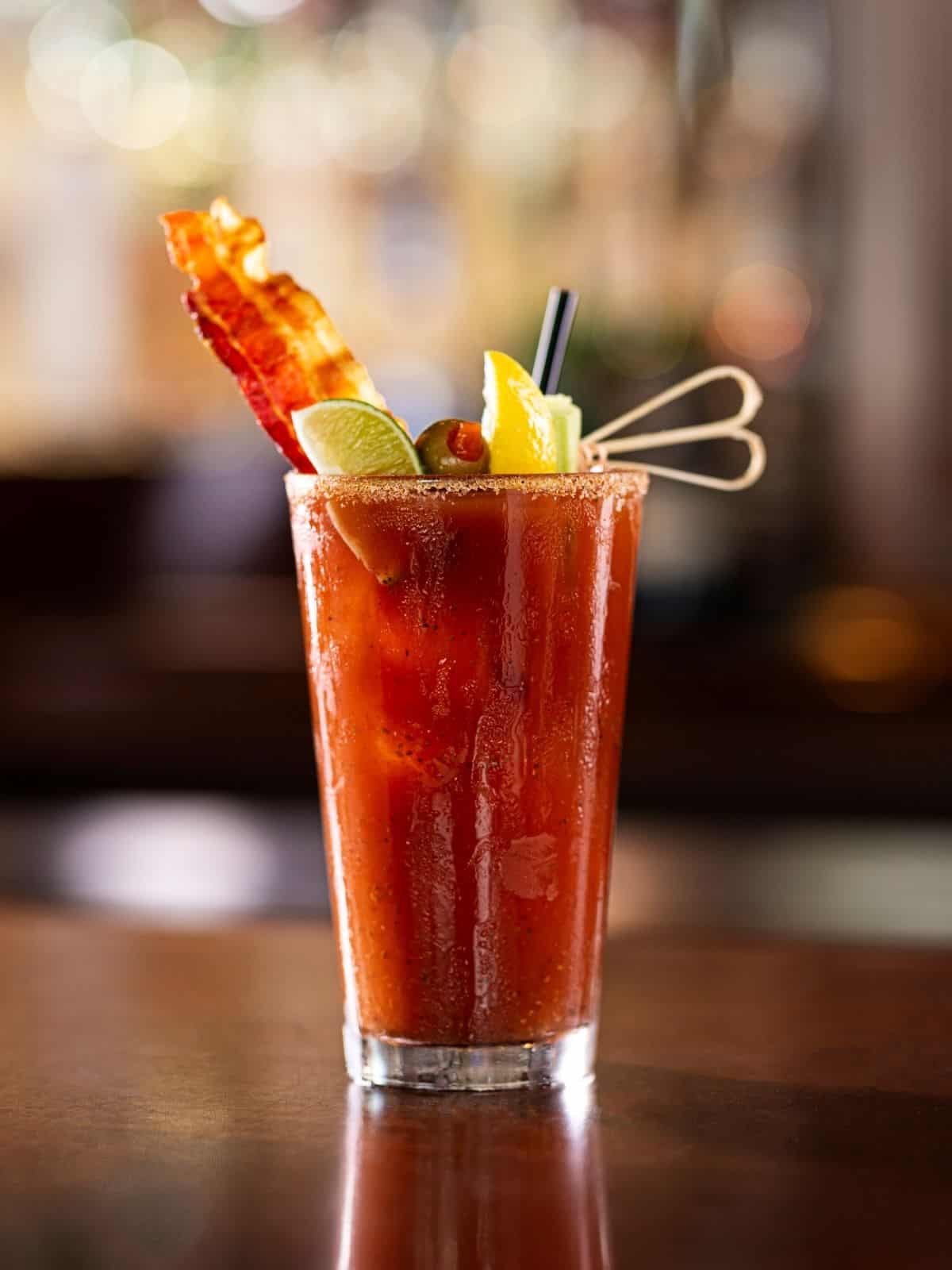 Tall bloody mary with lemon, lime, and bacon garnish.
