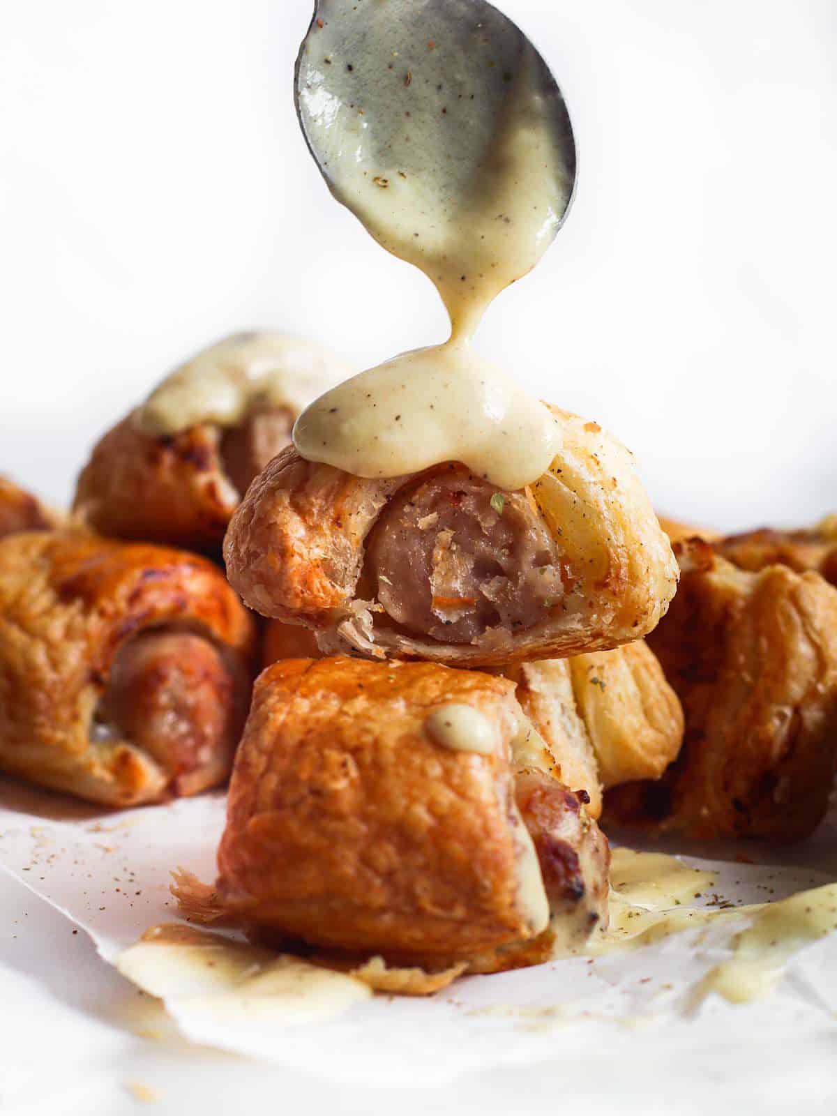 Puff pastry pigs in a blanket with sauce spooned over top.