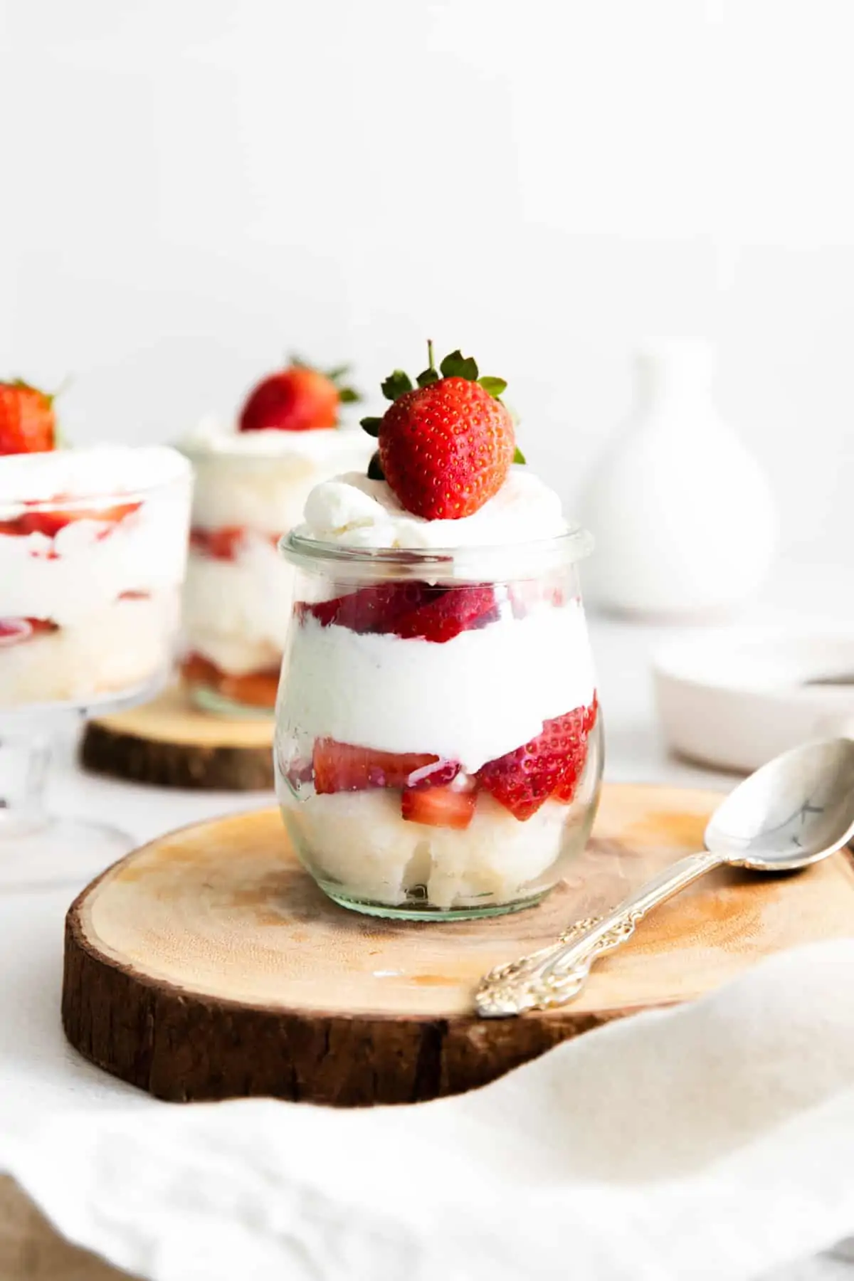 Strawberry shortcake trifle in a glass layered with cake, strawberries, whipped cream, and topped with a strawberry with a silver spoon on the side.