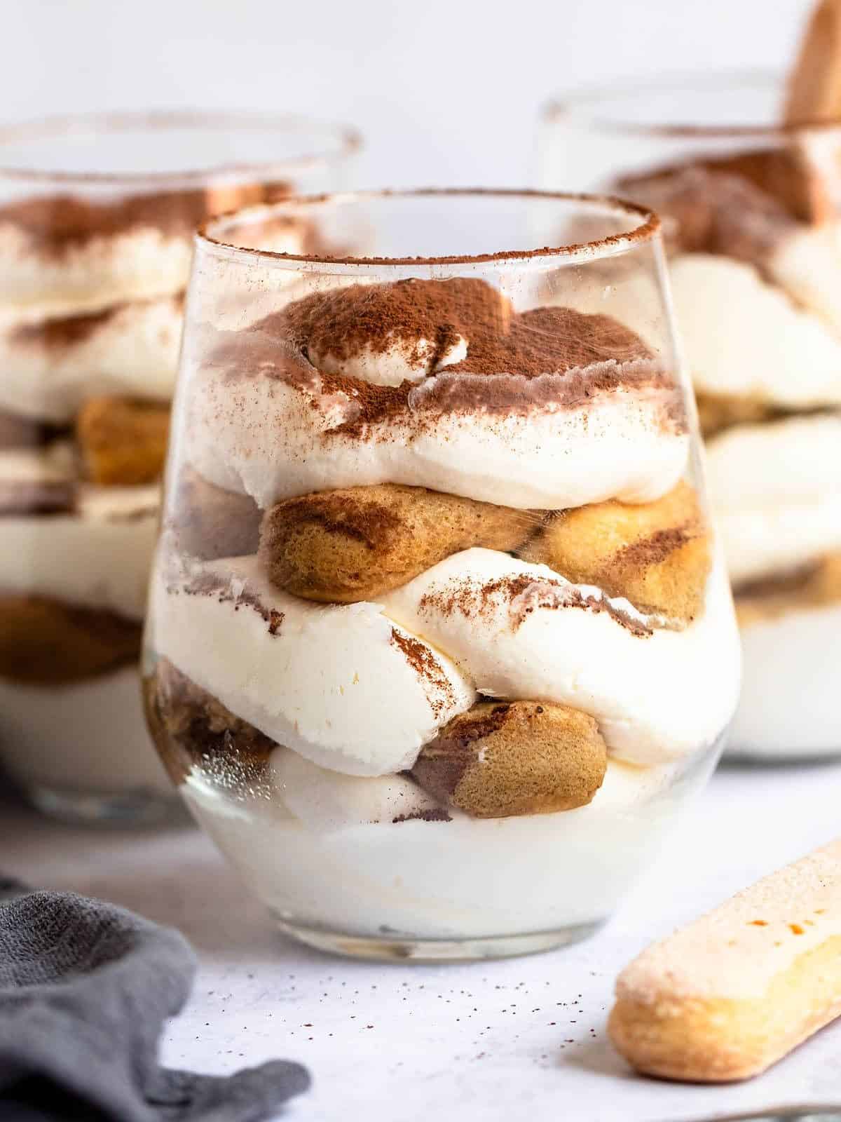 individual tiramisu dessert cups with layers of cream, lady fingers, and coffee in a glass.