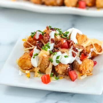 Loaded tater tots on a plate with cheese sour cream and bacon.